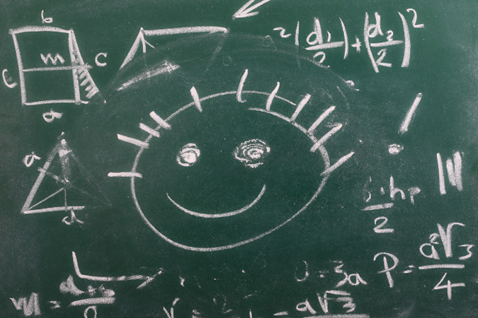 Eine grüne Tafel, auf der mit weißer Kreide verschiedene mathematische Formeln und geometrische Figuren skizziert sind. In der Mitte der Tafel befindet sich ein lächelnder Smiley mit großen Augen und einem fröhlichen Ausdruck.