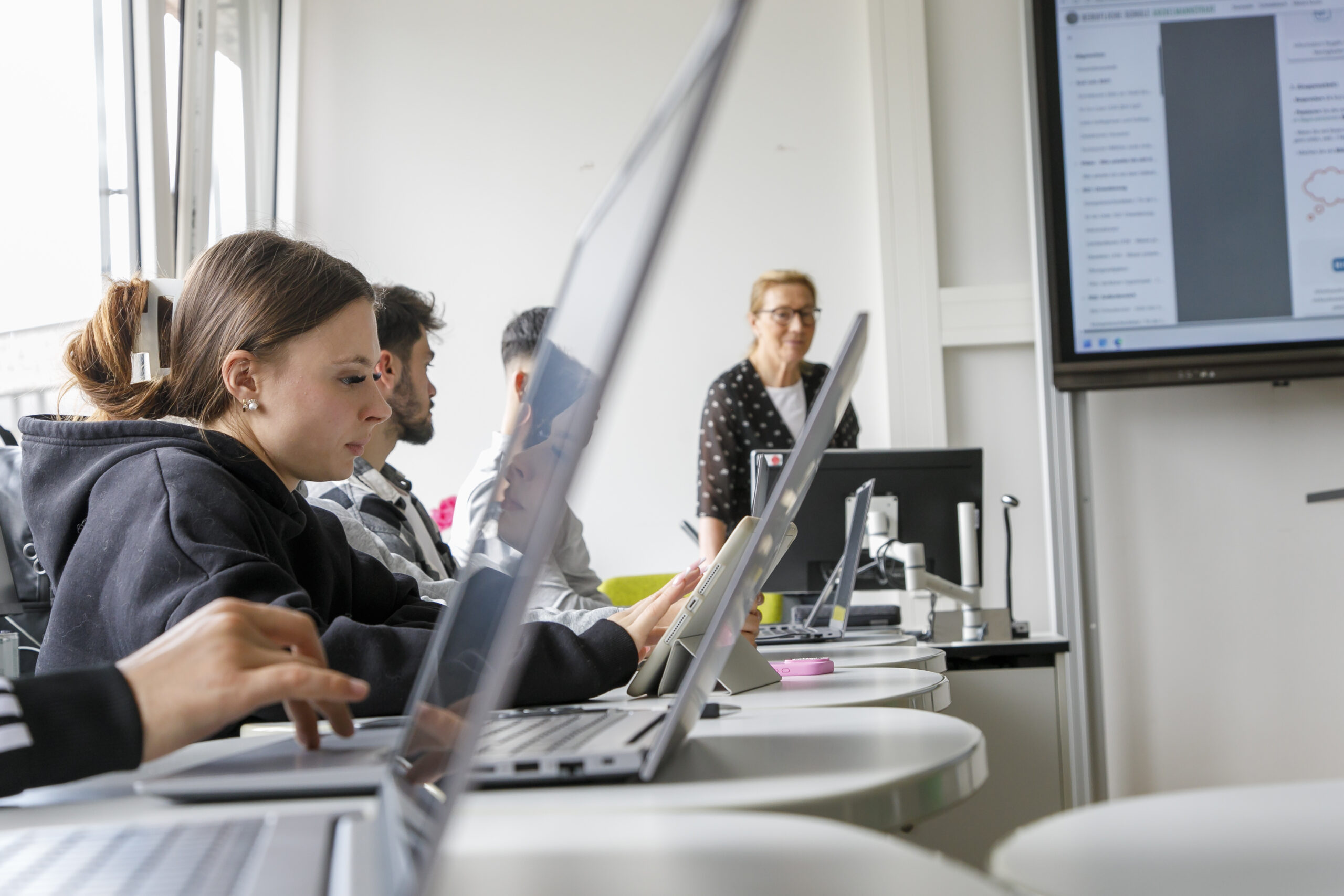 Schüler:innen mit Laptops und Lehrerin im Hintergrund